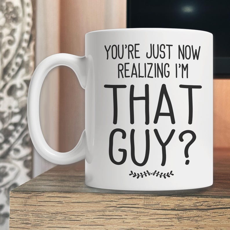 May include: White ceramic coffee mug with black text that reads "You're just now realizing I'm that guy?" with a small decorative flourish at the bottom.