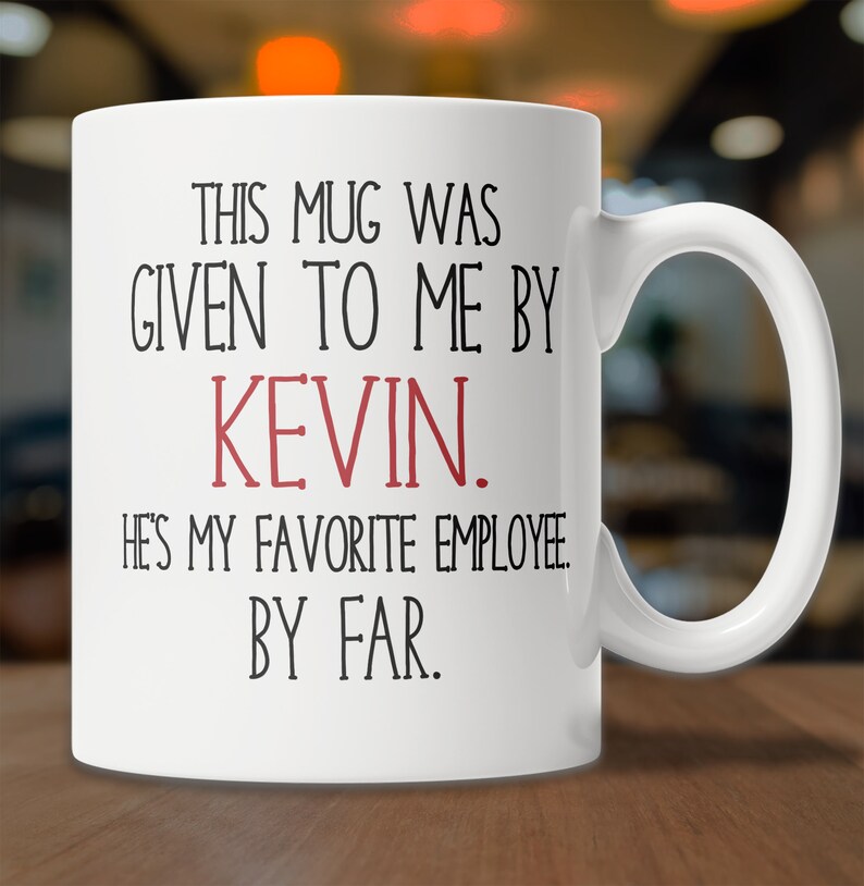 May include: White ceramic coffee mug with black text that reads "This mug was given to me by Kevin. He's my favorite employee. By far."