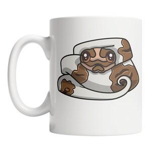 May include: White ceramic mug with a cartoon illustration of a brown and white snake curled up with its head peeking out. The snake has brown eyes and a brown mouth.