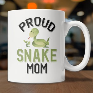 May include: White ceramic coffee mug with a green snake illustration and the text "PROUD SNAKE MOM" in black.
