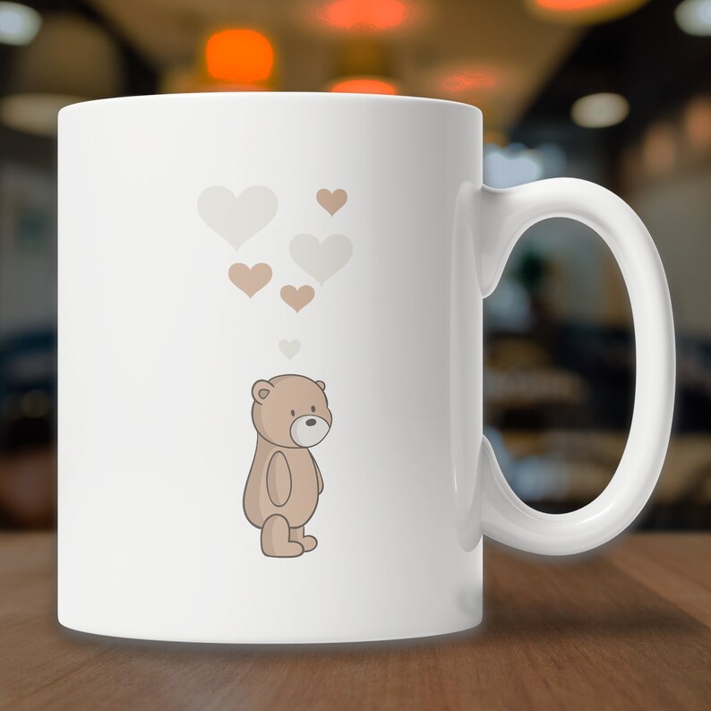 May include: White ceramic mug with a brown teddy bear illustration and a cluster of light brown and white hearts above the bear.