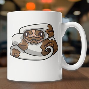 May include: White ceramic mug with a cartoon illustration of a brown and white snake curled up in a ball. The snake has large, round eyes and a cute expression.