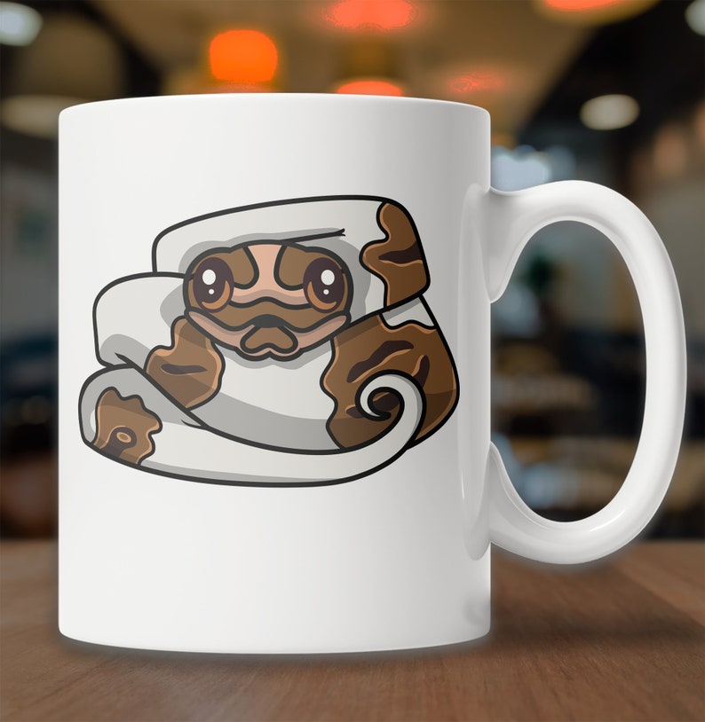 May include: White ceramic mug with a cartoon illustration of a brown and white snake curled up in a ball. The snake has large, round eyes and a cute expression.