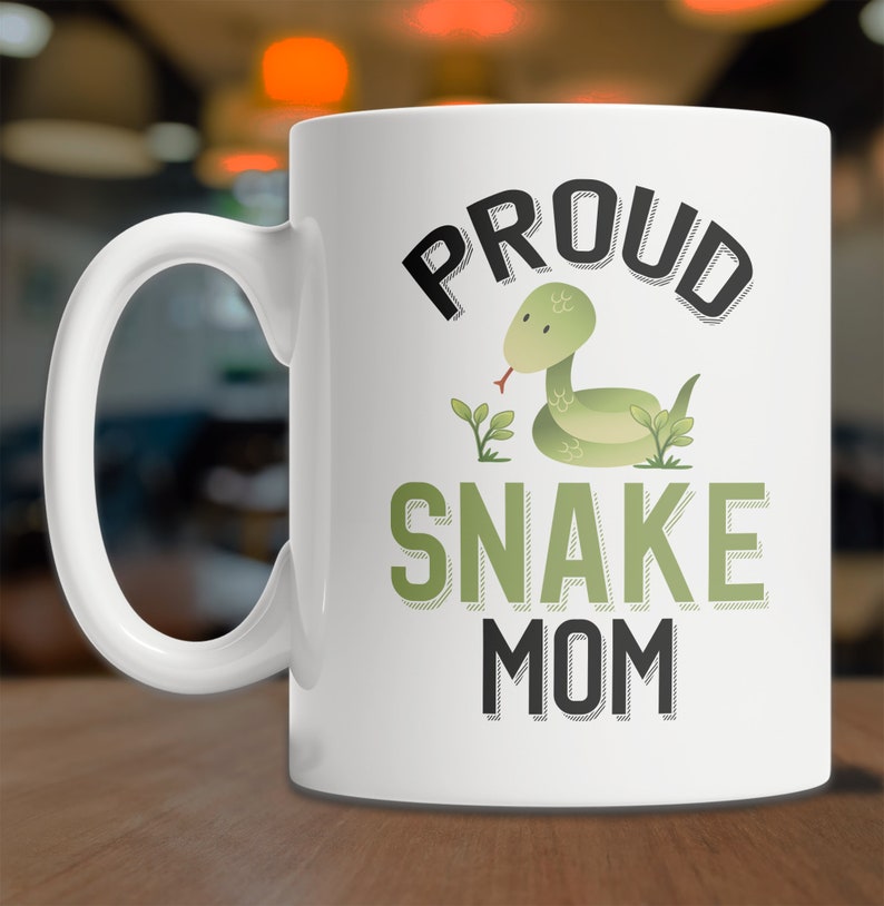 May include: White ceramic coffee mug with a black and green graphic design. The design features a green snake with a red tongue and the text "Proud Snake Mom".