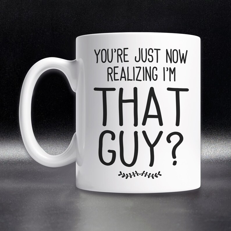 May include: White ceramic coffee mug with black text that reads "You're just now realizing I'm THAT GUY?" with a small decorative leaf design at the bottom.