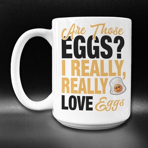 May include: White ceramic coffee mug with a black and gold design. The text on the mug reads "Are Those EGGS? I REALLY, REALLY LOVE Eggs".