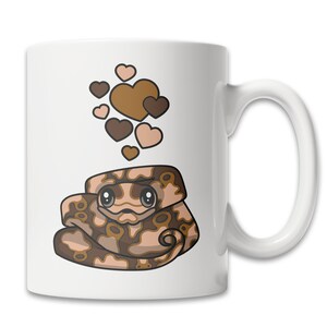 Peut inclure: Une tasse &agrave; caf&eacute; en c&eacute;ramique blanche avec une illustration de serpent brun et beige en dessin anim&eacute; avec des c&oelig;urs flottant au-dessus.