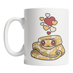 May include: White ceramic mug with a cartoon image of a yellow and white snake with red eyes. The snake is curled up and surrounded by small red and white hearts.
