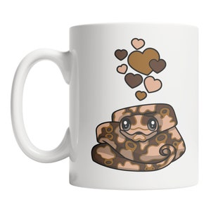 May include: White ceramic mug with a brown and tan cartoon snake with hearts above it. The snake has large eyes and is curled up. The hearts are brown and pink.