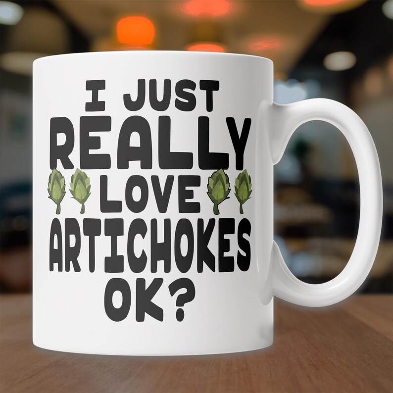 May include: White ceramic coffee mug with a black graphic that reads "I just really love artichokes ok?" with green artichoke illustrations.