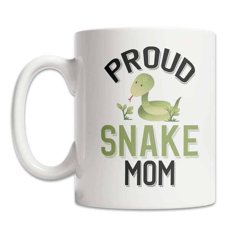 May include: White ceramic coffee mug with a black and green design. The design features the text "Proud Snake Mom" with a cartoon green snake in the middle.