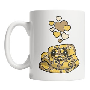 May include: White ceramic mug with a cartoon illustration of a yellow and brown snake with hearts floating above it. The snake has a cute face and is curled up.