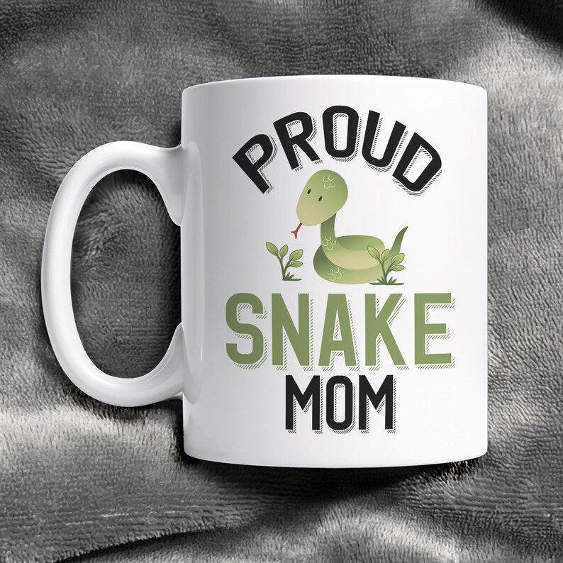 May include: White ceramic coffee mug with a black and green graphic design. The design features a cartoon snake with the text "Proud Snake Mom".