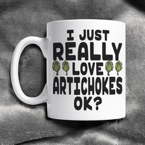 May include: White ceramic coffee mug with a black graphic that says "I just really love artichokes ok?" with three green artichoke illustrations.
