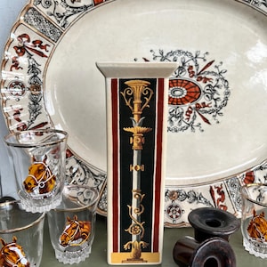 May include: A selection of vintage items, including a rectangular vase with a black and gold design, shot glasses with horse graphics, a large oval platter, and two dark brown objects. The vase has red stripes.