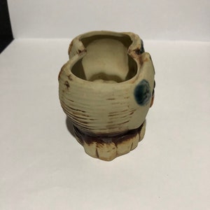 May include: A ceramic planter with two separate compartments, each with a rounded opening. The planter is decorated with brown and blue glaze, creating a rustic and whimsical look.