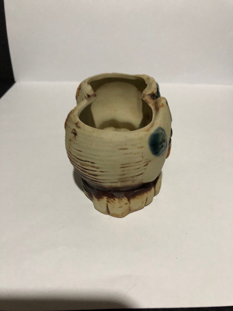 May include: A ceramic planter with two separate compartments, each with a rounded opening. The planter is decorated with brown and blue glaze, creating a rustic and whimsical look.