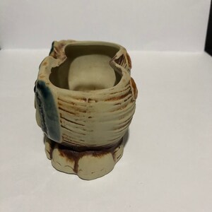 May include: A ceramic owl planter with two separate compartments. The owl is painted in shades of brown, beige, and blue. The planter has a textured surface and a rounded base.