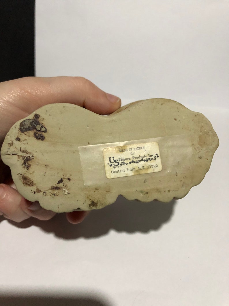 May include: A white ceramic figurine of a dog with a label on the bottom that reads "Made in Taiwan for U.S. Leisure Products Inc. Central Islip, N.Y. 11722"