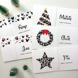 May include: A collection of white rectangular Christmas cards featuring personalised names including Amy, Jas, Maisie, Ollie, and Fin. The designs incorporate black mouse-ear silhouettes, red bows, candy canes, and festive shapes arranged into trees, wreaths, and stars.