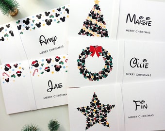 May include: A collection of white rectangular Christmas cards featuring personalized names including Amy, Jas, Maisie, Ollie, and Fin. The designs incorporate black mouse-ear silhouettes, red bows, candy canes, and festive shapes arranged into trees, wreaths, and stars.