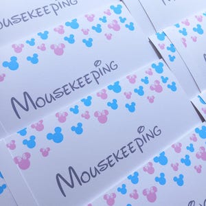 May include: A collection of white rectangular envelopes featuring the word MOUSEKEEPING printed in a dark gray script font. The envelopes are decorated with a repeating pattern of small light blue and pink mouse head silhouettes.
