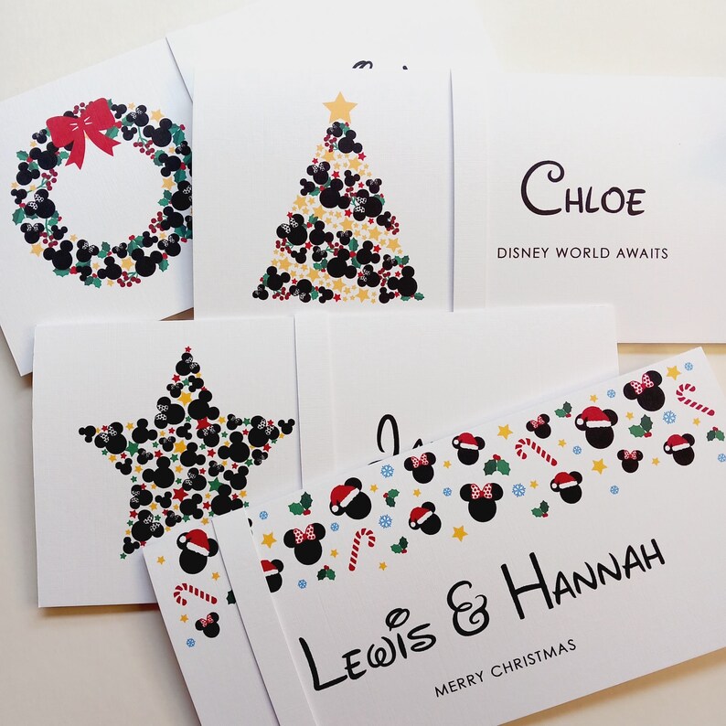May include: A collection of white greeting cards featuring festive designs with black mouse-ear silhouettes, red bows, holly, and stars. One card displays the text Chloe Disney World Awaits, and another shows Lewis & Hannah Merry Christmas.