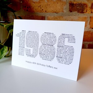 May include: A white rectangular greeting card featuring black printed text detailing historical facts from 1986, including popular films, music, books, and news. The bottom of the card displays the text, Happy 40th Birthday Toffers xxx.