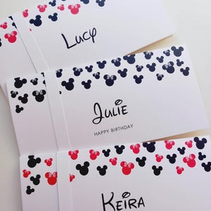 May include: Three white rectangular cards featuring a pattern of black and pink mouse head silhouettes along the top edge. The cards are personalized with the names Lucy, Julie, and Keira in black script, with Happy Birthday printed below Julie.