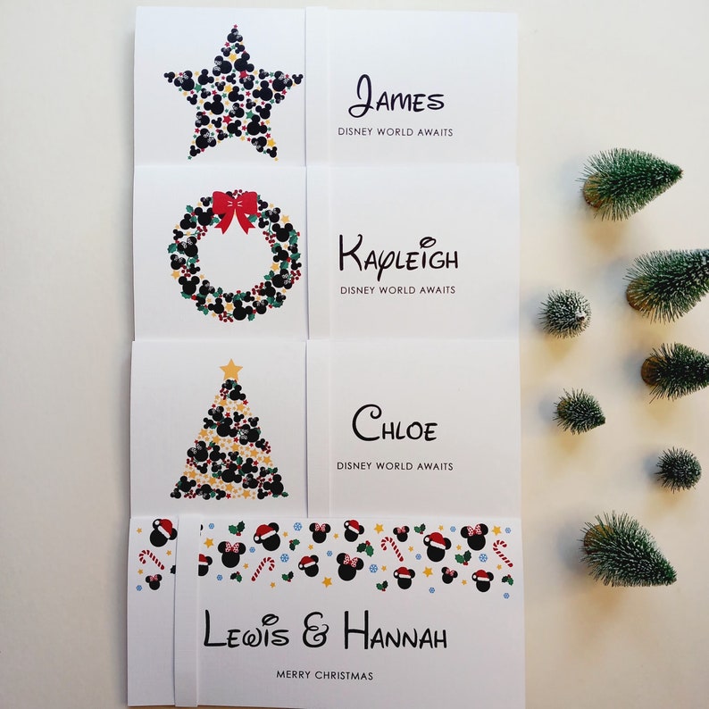 May include: Four white rectangular cards featuring festive holiday graphics made of black mouse-ear silhouettes. The cards display the names James, Kayleigh, Chloe, and Lewis & Hannah, with the text Disney World Awaits or Merry Christmas printed.
