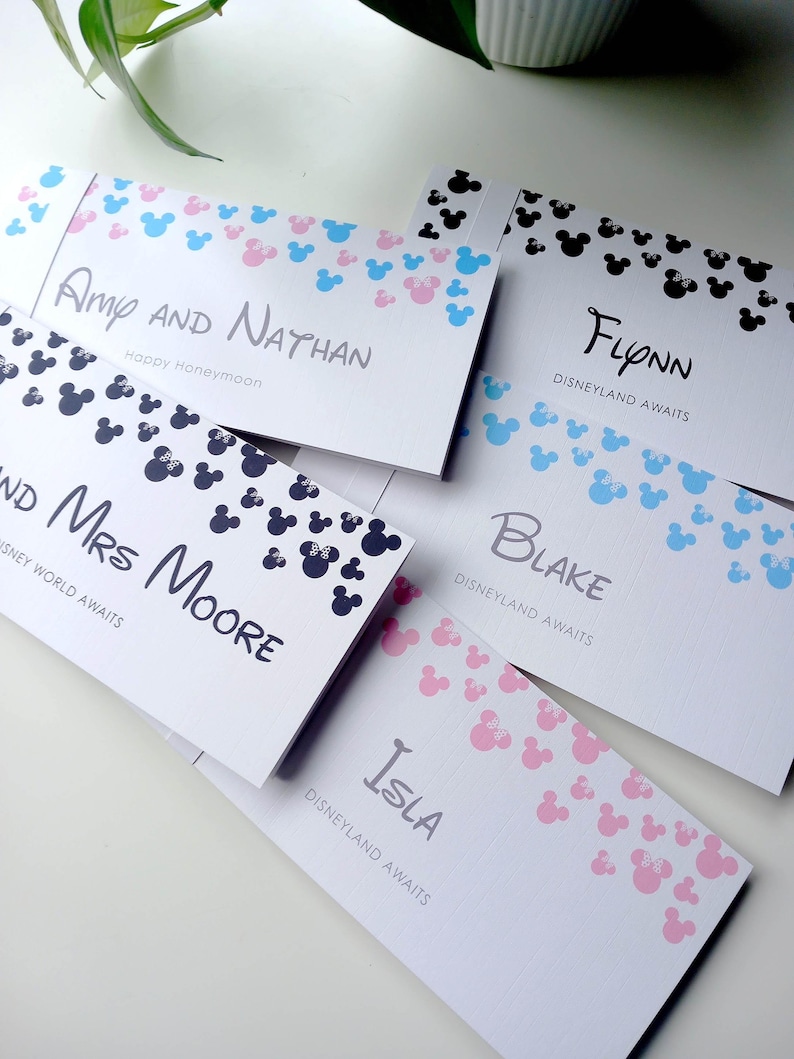 May include: Five rectangular white paper envelopes featuring various patterns of small mouse-ear silhouettes in pink, blue, and black. Each envelope is personalized with names such as Amy and Nathan, Flynn, Mrs. Moore, Blake, and Isla, along with text like Disneyland Awaits.