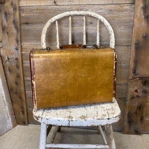 May include: A vintage rectangular suitcase with a textured mustard-yellow exterior and dark brown trim. The suitcase features a brown plastic handle, two metallic latches on the top edge, and visible signs of wear along the edges and corners.