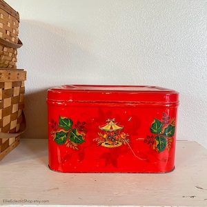 May include: A rectangular red tin with a lid, decorated with a carousel and floral design. The tin has a glossy finish and is sitting on a white surface. The text "EllieEclecticShop.etsy.com" is visible.