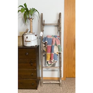 May include: A wooden ladder leaning against a wall with a colorful crocheted blanket draped over it. The ladder has a rustic, vintage look and is perfect for displaying items.