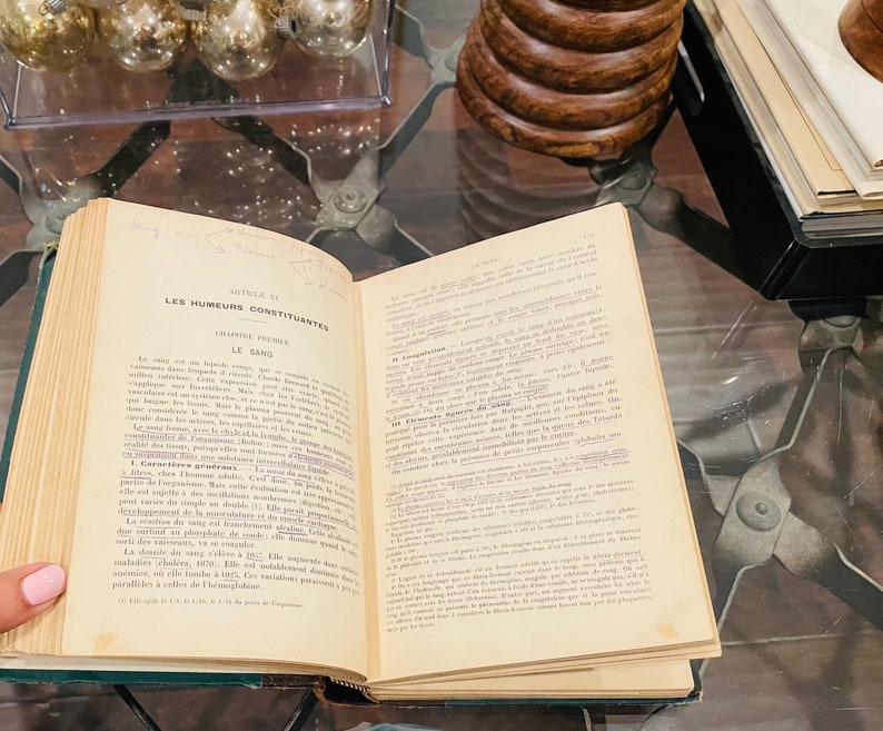 May include: An open book with a yellowed page, titled "Les Humeurs Constituantes" and "Le Sang." The text is in French and discusses the components of blood.