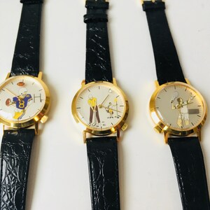 May include: Three gold-toned watches with black leather straps. Each watch face features a different sport: football, golf, and tennis. The watch faces have a white background with colorful illustrations of athletes.