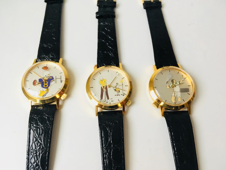 May include: Three gold-toned watches with black leather straps. Each watch face features a different sport: football, golf, and tennis. The watch faces have a white background with colorful illustrations of athletes.