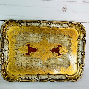 May include: A gold and white decorative tray with an ornate design. The tray has a scalloped edge and a raised center with a floral pattern.