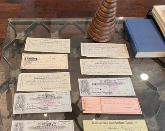 May include: A collection of vintage bank checks from different banks, including First National Bank, American Union Bank, and Harris Trust and Savings Bank. The checks are on a glass table with a wooden stacking toy in the background.