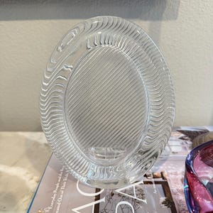 May include: A clear glass oval picture frame with a wavy design around the edge and a striped pattern inside the frame.