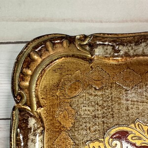 May include: A decorative tray with a gold and brown finish. The tray has a raised, ornate border and a textured surface with a floral design.