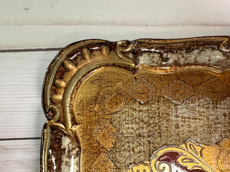 May include: A decorative tray with a gold and brown finish. The tray has a raised, ornate border and a textured surface with a floral design.