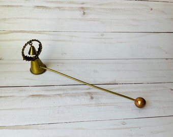 May include: A vintage brass bell with a long handle and a round ball at the end. The bell has a conical shape with a decorative twisted wire ring around the top. The handle extends from the bell's base, and the ball is a solid sphere.