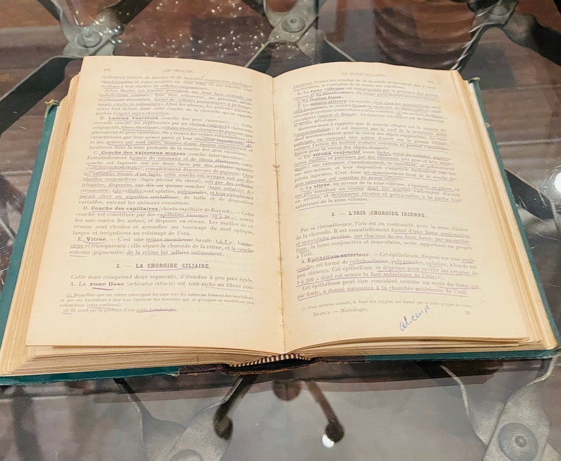 May include: An open book with yellowed pages and a green cover. The book is titled "La Choroide Celiatre" and "L'Iris Choroide" with text in French. The book is open to a page with the text "La Choroide Celiatre" and "L'Iris Choroide" highlighted in blue.