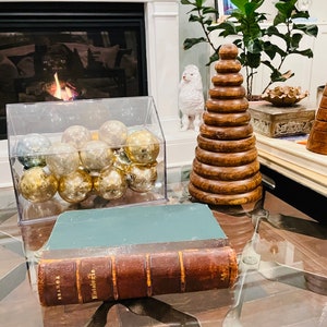 May include: A glass container filled with gold and silver Christmas ornaments sits on a glass coffee table next to a wooden stacking toy and a leather-bound book titled "Histologie".