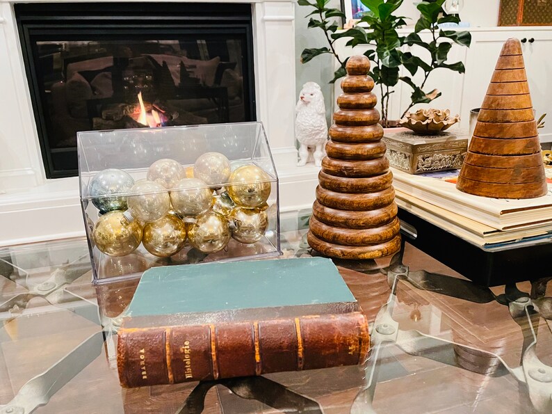May include: A glass container filled with gold and silver Christmas ornaments sits on a glass coffee table next to a wooden stacking toy and a leather-bound book titled "Histologie".