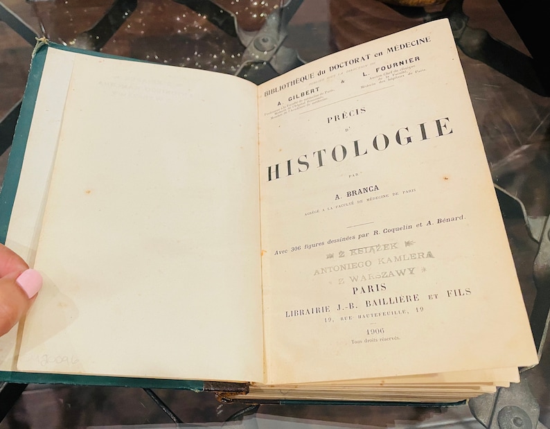 May include: A vintage book titled "Precis d'Histologie" by A. Branca. The book is bound in green leather and has a gold-embossed title on the cover. The book is open to the title page, which includes the author's name, the publisher's name, and the year of publication.