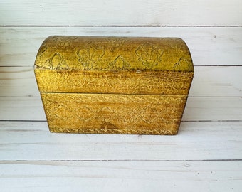 May include: A gold wooden box with an ornate design. The box has a hinged lid and is decorated with a floral pattern.