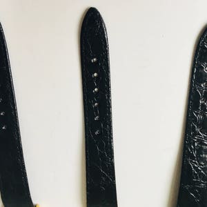 May include: Three black watch straps with varying textures and designs. The straps are made of a leather-like material and have holes for adjustment. The straps are displayed against a white background.