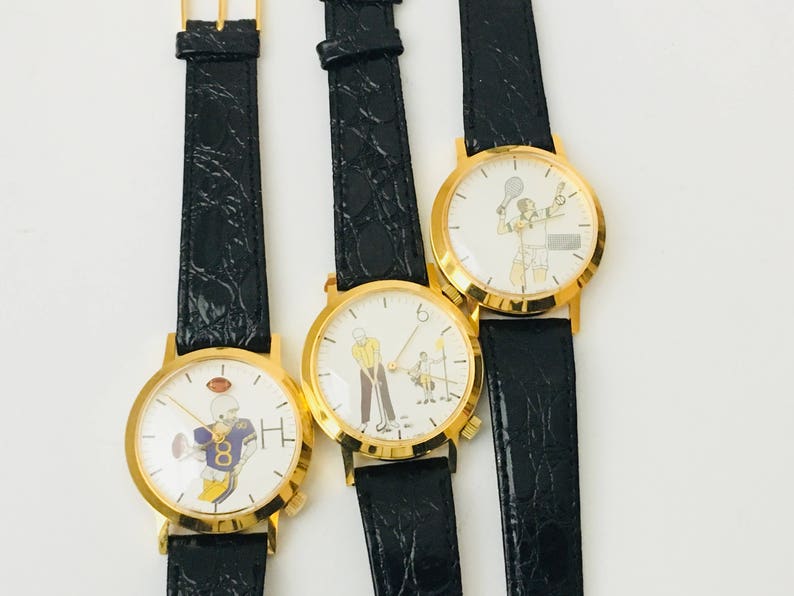 May include: Three gold-toned watches with black leather bands. Each watch face features a different sport: football, golf, and tennis. The football watch has a player in a purple and gold uniform. The golf watch shows a golfer. The tennis watch has a tennis player.